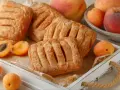 Chrupiące ciasto francuskie z morelami, ułożone na drewnianej tacy, obok świeżych owoców.