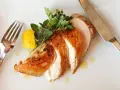 Soczysty kurczak sous vide, pokrojony w plastry, z cytryną i ziołami, na białym talerzu. Obok widelec i nóż.