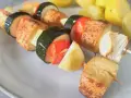 Szaszłyki z tofu, cukinii, papryki i cebuli na talerzu, obok gotowane ziemniaki.