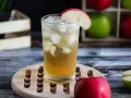 Orzeźwiające drinki z sokiem jabłkowym, ozdobione plasterkiem jabłka, z lodem i jabłkami w tle.
