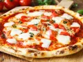 Pyszne ciasto na pizzę bez wyrastania, z pomidorami, mozzarellą i bazylią, na drewnianej desce.
