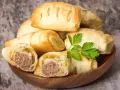 Stos pieczonego ciasta francuskiego z kiełbasą w środku, ozdobione gałązką pietruszki. Idealne na szybką przekąskę.