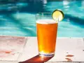 Orzeźwiający drink z piwem i plasterkiem limonki, stojący na brzegu basenu. Idealny na upalne dni.
