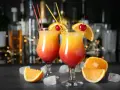 Dwa drinki z wódką, udekorowane pomarańczą i wiśnią, z kostkami lodu i owocami na blacie. Idealne domowe drinki z wódką na letnie wieczory.
