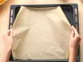 Ręce układają papier do pieczenia na blasze. Zastanawiasz się, czym zastąpić papier do pieczenia? Oto praktyczne rozwiązanie!