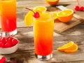 Dwa drinki z whisky i sokiem pomarańczowym, ozdobione wiśniami i plasterkami pomarańczy, na drewnianym stole.
