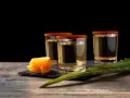 Trzy kieliszki z mezcalem, ozdobione solą i chili, obok pomarańczy i liścia agawy. Chcesz wiedzieć, mezcal co to?