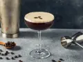 Elegancki drink z kawą, ozdobiony ziarnami kawy, obok shakera i miarki barmańskiej. Idealny na pobudzenie.