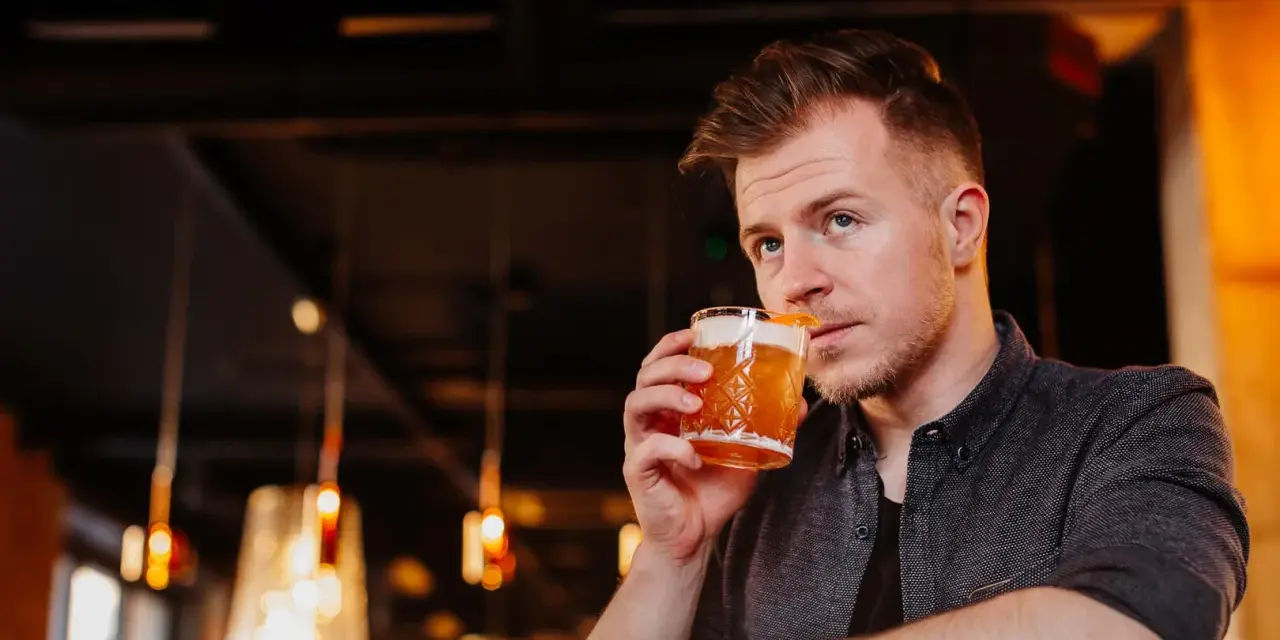 Mężczyzna sączy orzeźwiający whisky sour, delektując się smakiem w nastrojowym barze.