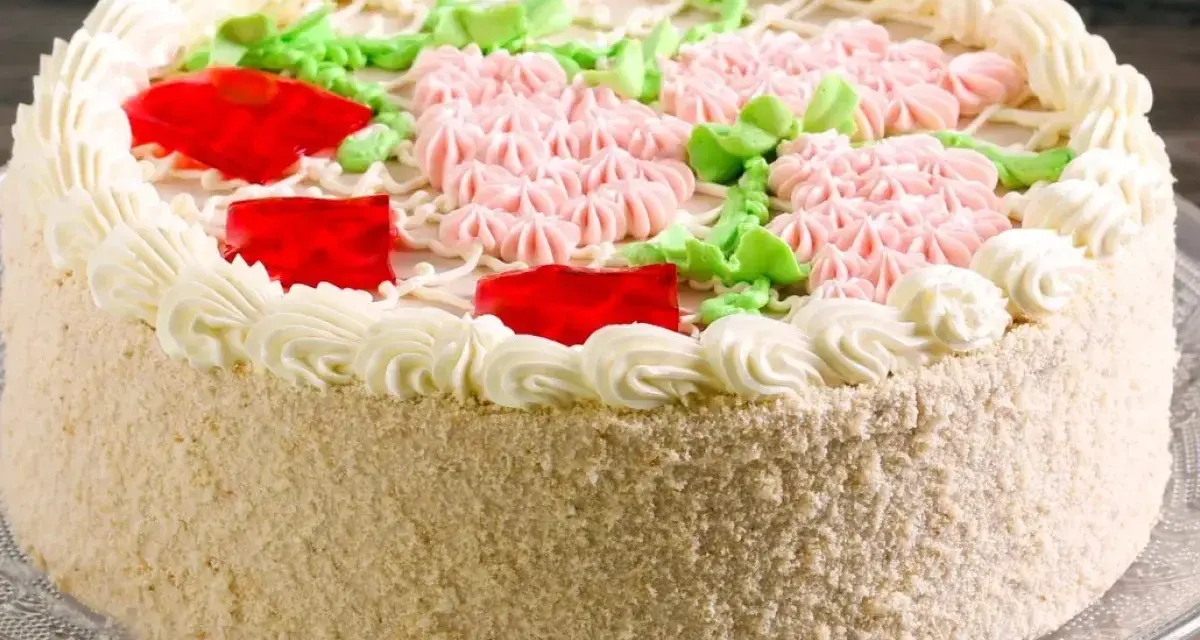 Elegancki tort udekorowany kremem, różowymi kwiatkami, zielonymi listkami i czerwonymi galaretkami. Pyszny krem do tortu zachwyca smakiem.