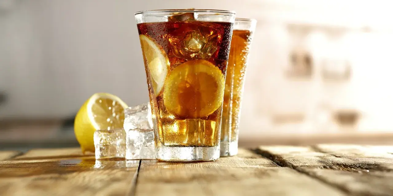 Dwa orzeźwiające drinki Long Island Iced Tea z plasterkami cytryny i lodem na drewnianym blacie.
