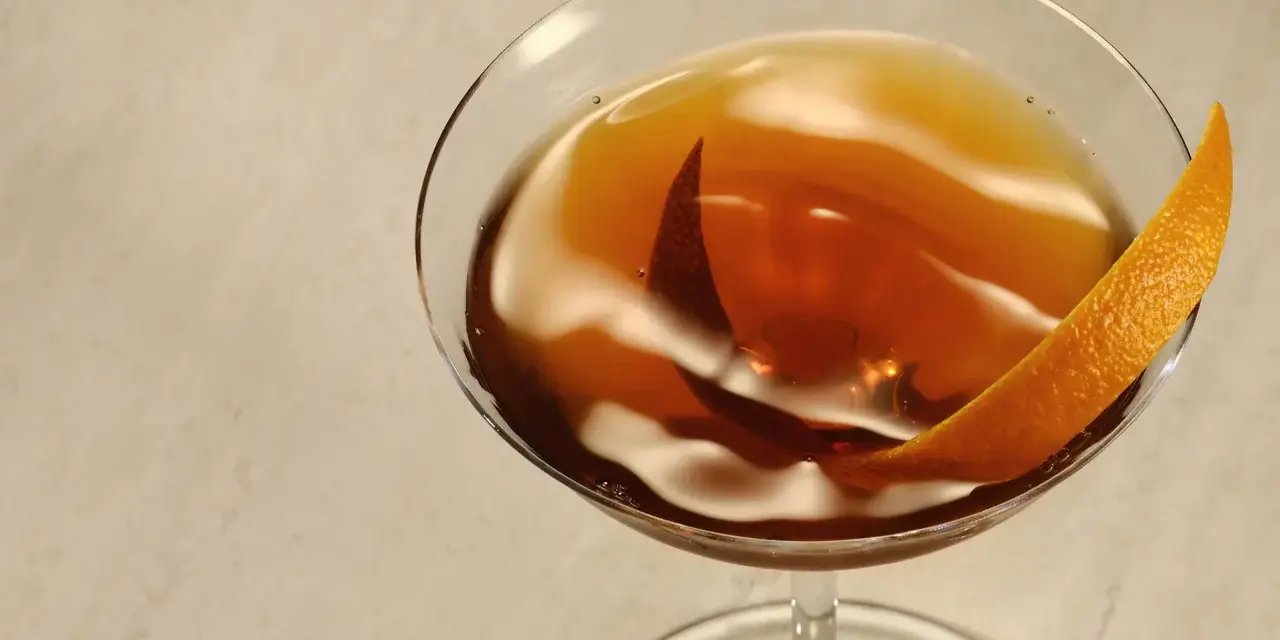 Elegancki Rob Roy cocktail w kieliszku, ozdobiony skórką pomarańczy.