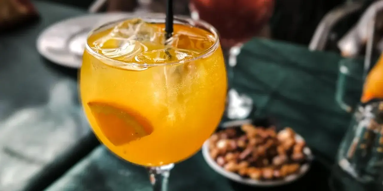 Orzeźwiający drink agua de valencia z plasterkiem pomarańczy i lodem, na stole obok miseczki z orzeszkami.