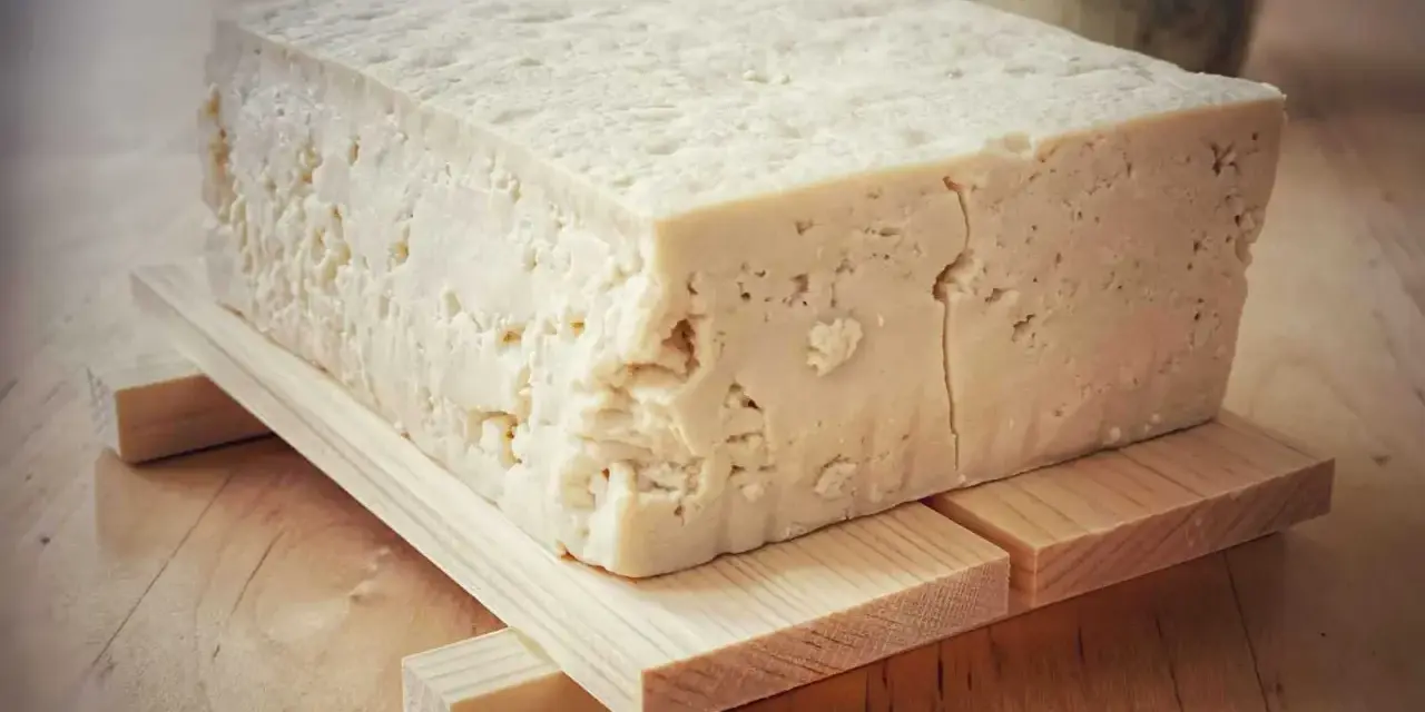 Kostka białego tofu, zrobionego z soi, na drewnianej podstawce.