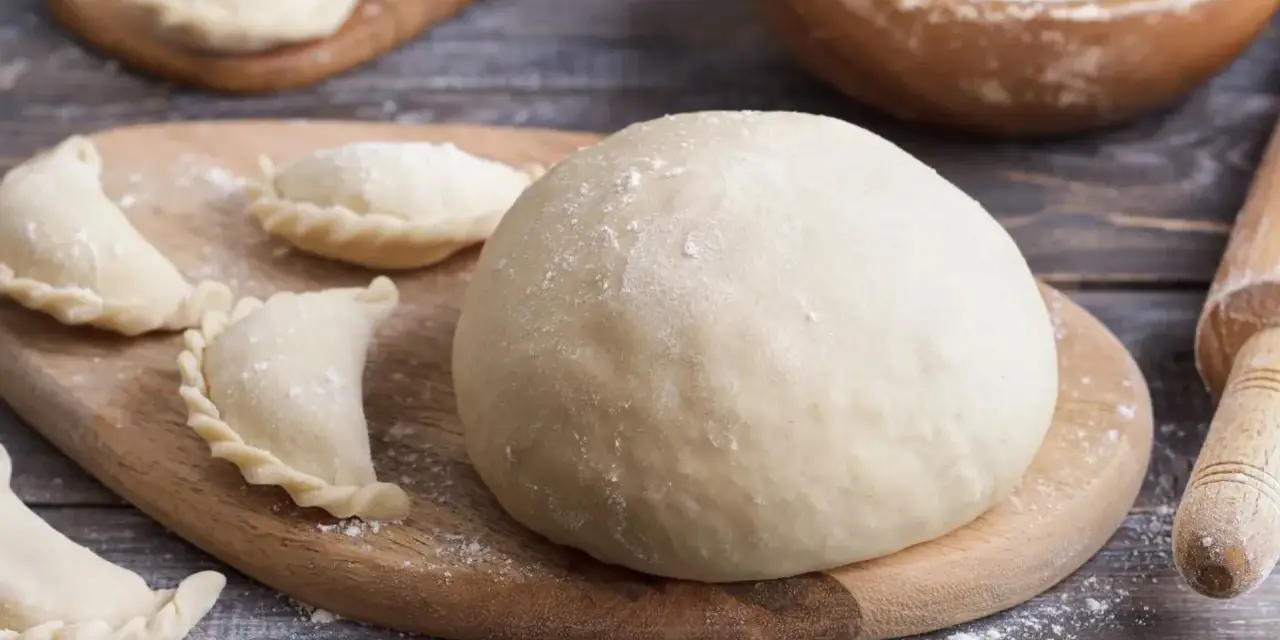 Gotowe ciasto na pierogi i kilka uformowanych pierożków na desce. Czy ciasto na pierogi można zrobić dzień wcześniej? Tak, można!
