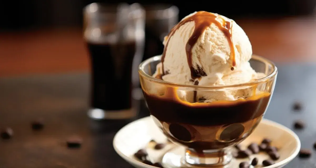 Lody waniliowe z syropem karmelowym w pucharku, obok szklaneczki z ciemnym napojem. Idealne połączenie, gdy zastanawiasz się, **Baileys z czym pić**.