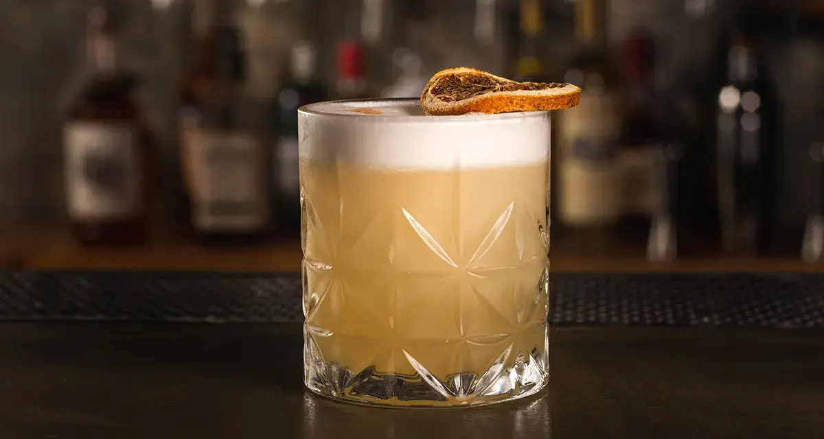 Idealny drink whisky sour z pianką i plasterkiem suszonej pomarańczy, gotowy do degustacji.