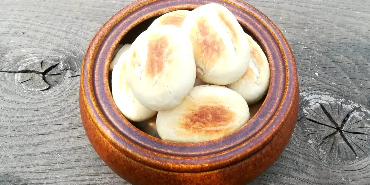 Małe, okrągłe bułki z ciasta na pizzę, lekko zarumienione, w brązowej misce na drewnianym stole.