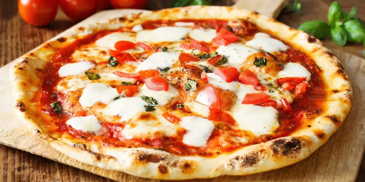 Pyszne ciasto na pizzę bez wyrastania, z pomidorami, mozzarellą i bazylią, na drewnianej desce.