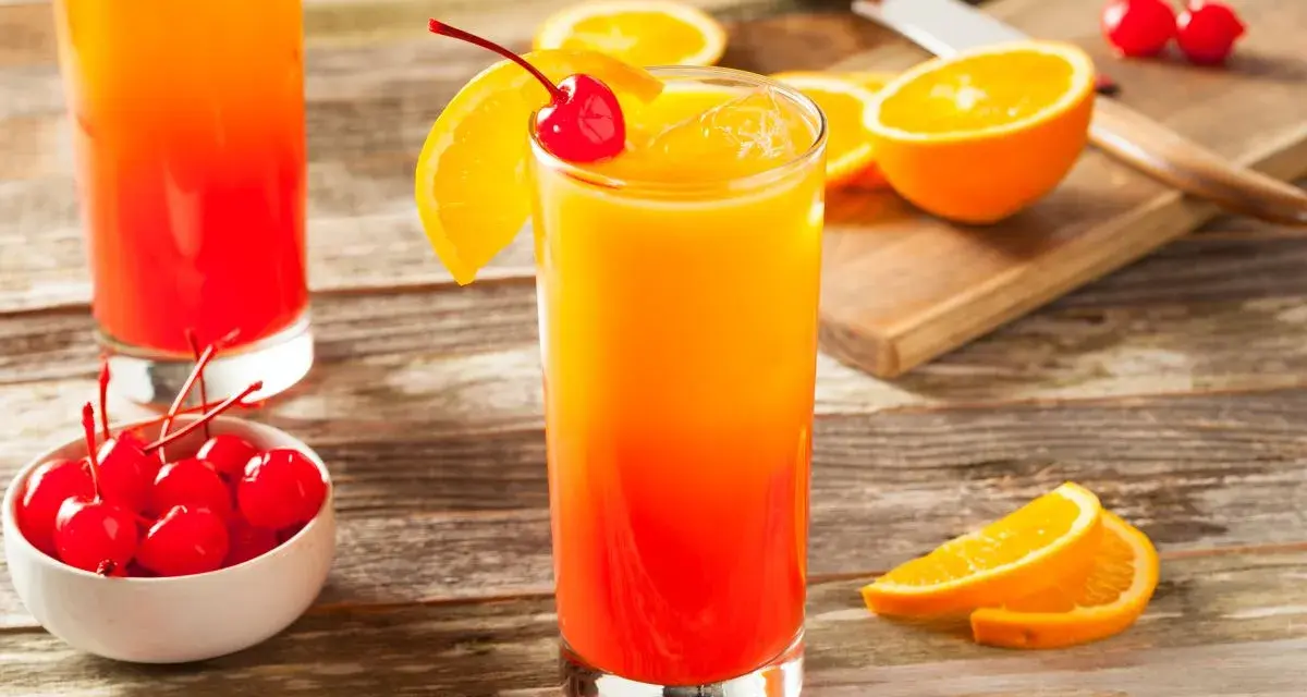 Dwa drinki z grenadyną, ozdobione plasterkami pomarańczy i wiśniami, stoją na drewnianym stole.