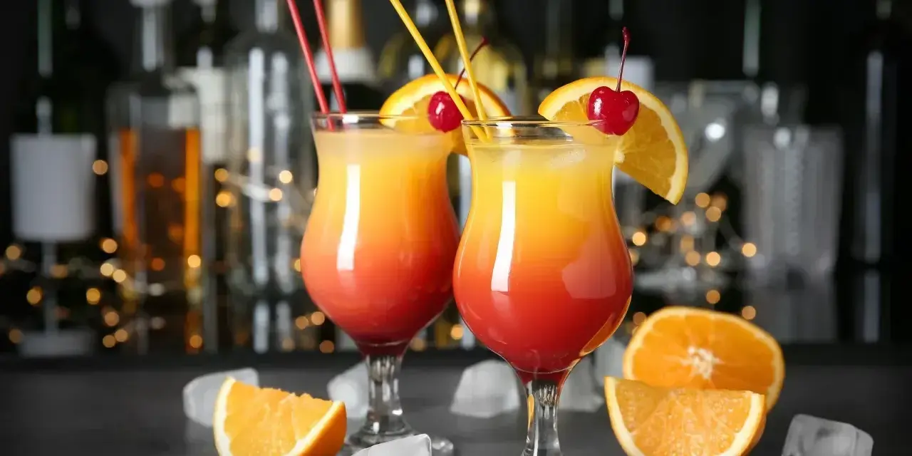 Dwa drinki z wódką, udekorowane pomarańczą i wiśnią, z kostkami lodu i owocami na blacie. Idealne domowe drinki z wódką na letnie wieczory.