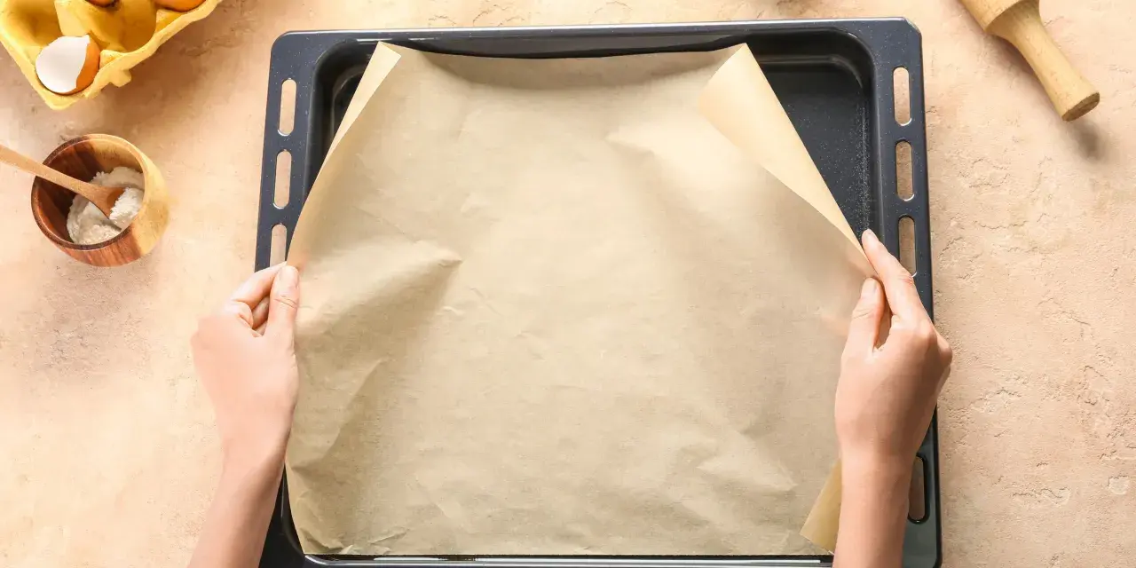 Ręce układają papier do pieczenia na blasze. Zastanawiasz się, czym zastąpić papier do pieczenia? Oto praktyczne rozwiązanie!