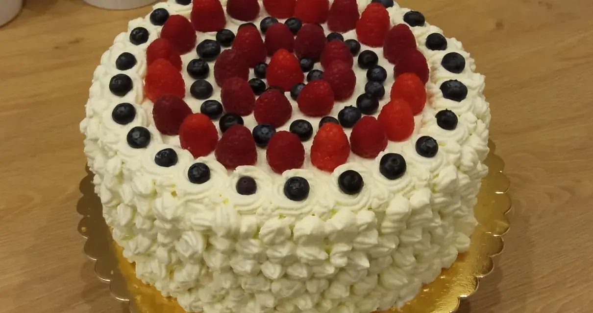 Pyszny tort bezglutenowy ozdobiony bitą śmietaną, malinami i borówkami. Idealny na każdą okazję, a przepis na niego jest prosty!