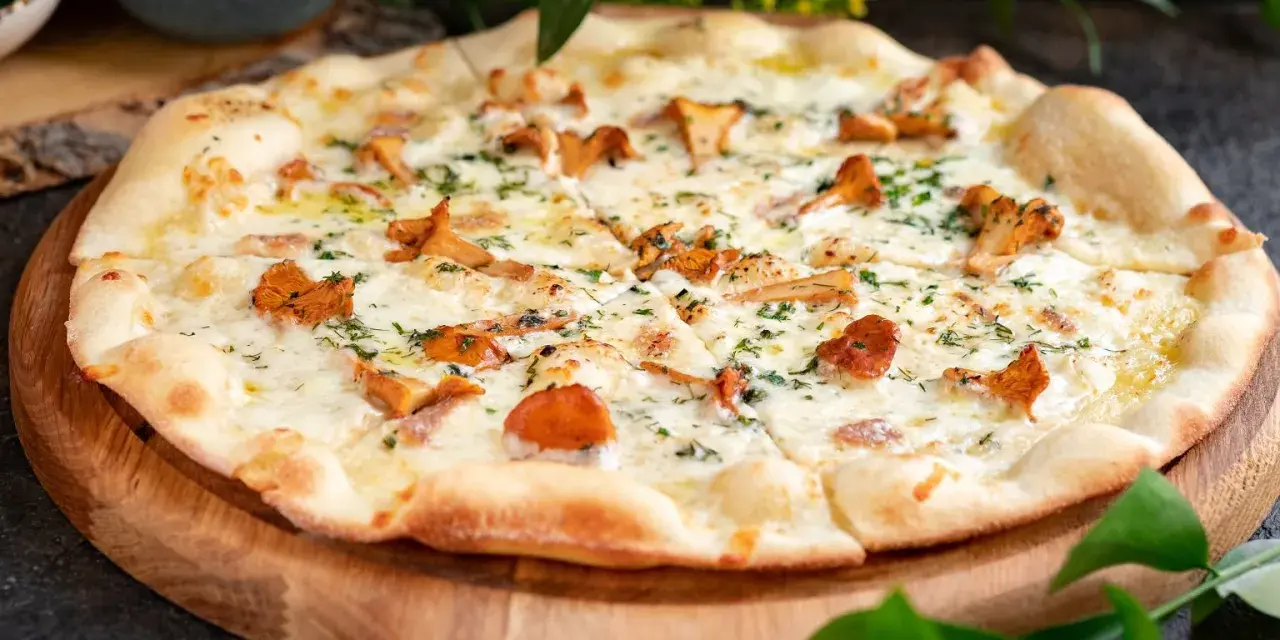 Pyszna pizza z kurkami, roztopionym serem i ziołami, podana na drewnianej desce.
