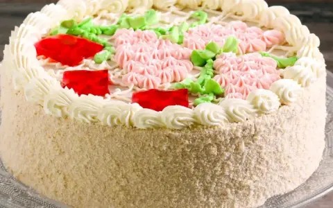 Elegancki tort udekorowany kremem, różowymi kwiatkami, zielonymi listkami i czerwonymi galaretkami. Pyszny krem do tortu zachwyca smakiem.