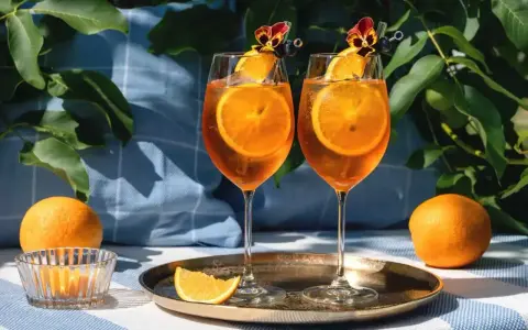 Dwa orzeźwiające drinki z aperolem i sokiem pomarańczowym, ozdobione plastrami pomarańczy i kwiatami, gotowe na letnie popołudnie.
