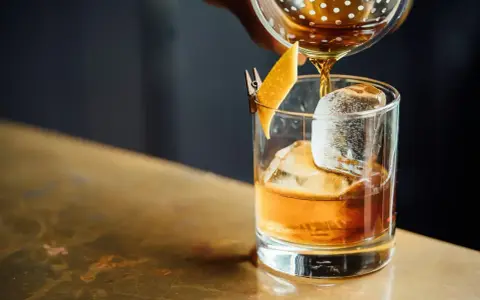 Idealny wieczór: nalewanie whisky z colą do szklanki z lodem i skórką pomarańczy.