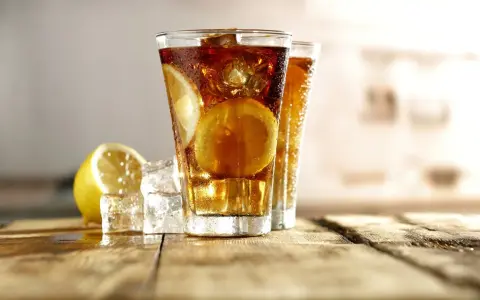 Dwa orzeźwiające drinki Long Island Iced Tea z plasterkami cytryny i lodem na drewnianym blacie.