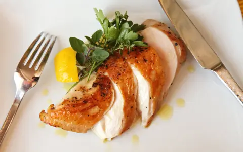 Soczysty kurczak sous vide, pokrojony w plastry, z cytryną i ziołami, na białym talerzu. Obok widelec i nóż.