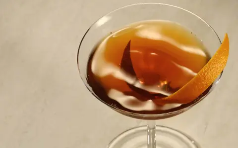 Elegancki Rob Roy cocktail w kieliszku, ozdobiony skórką pomarańczy.