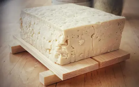 Kostka białego tofu, zrobionego z soi, na drewnianej podstawce.