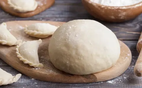 Gotowe ciasto na pierogi i kilka uformowanych pierożków na desce. Czy ciasto na pierogi można zrobić dzień wcześniej? Tak, można!