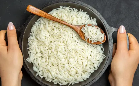 Dwie ręce trzymają okrągłą, czarną patelnię pełną puszystego ryżu basmati. Drewniana łyżka zanurzona w ryżu.