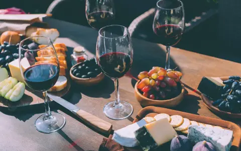 Degustacja wina merlot: jakie to wino? Kieliszki pełne rubinowego trunku, deska serów, winogrona, oliwki i figi tworzą idealną kompozycję.