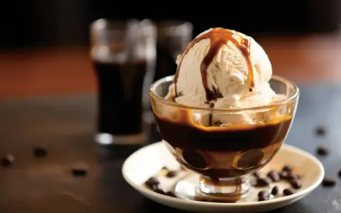 Lody waniliowe z syropem karmelowym w pucharku, obok szklaneczki z ciemnym napojem. Idealne połączenie, gdy zastanawiasz się, **Baileys z czym pić**.