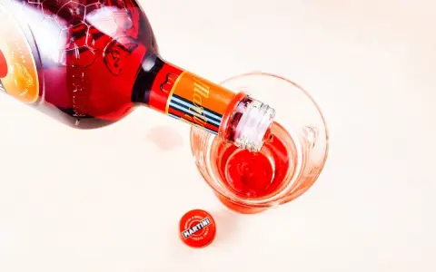 Czerwony Martini Fiero drink nalewany z butelki do szklanki. Obok leży czerwona zakrętka z logo Martini.
