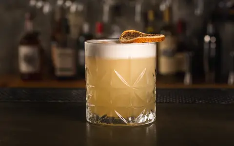 Idealny drink whisky sour z pianką i plasterkiem suszonej pomarańczy, gotowy do degustacji.