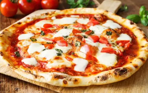 Pyszne ciasto na pizzę bez wyrastania, z pomidorami, mozzarellą i bazylią, na drewnianej desce.