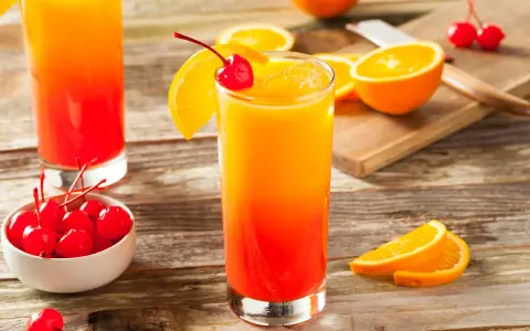 Dwa drinki z grenadyną, ozdobione plasterkami pomarańczy i wiśniami, stoją na drewnianym stole.