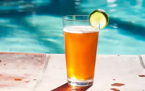Orzeźwiający drink z piwem i plasterkiem limonki, stojący na brzegu basenu. Idealny na upalne dni.