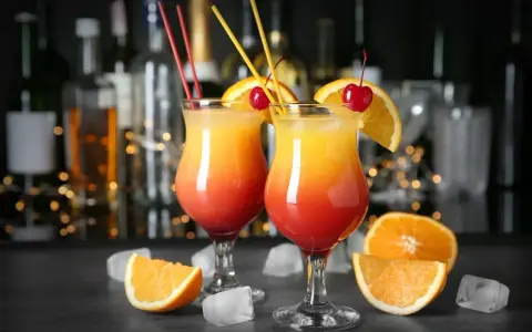 Dwa drinki z wódką, udekorowane pomarańczą i wiśnią, z kostkami lodu i owocami na blacie. Idealne domowe drinki z wódką na letnie wieczory.