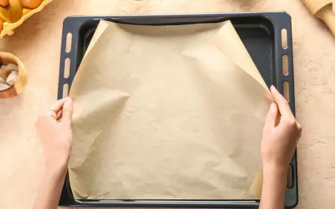 Ręce układają papier do pieczenia na blasze. Zastanawiasz się, czym zastąpić papier do pieczenia? Oto praktyczne rozwiązanie!