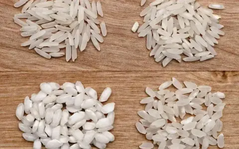 Cztery rodzaje ryżu, w tym ryż do risotto, ułożone na drewnianym tle.