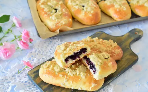 Pyszne jagodzianki z kruszonką, jedna przekrojona, ukazująca soczyste jagody. Obok różowe róże.