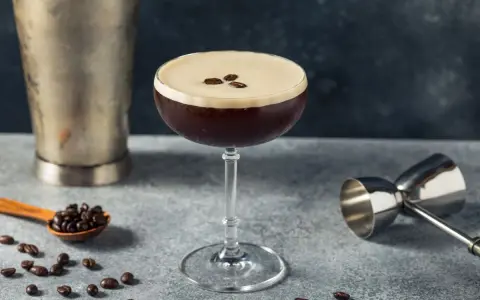 Elegancki drink z kawą, ozdobiony ziarnami kawy, obok shakera i miarki barmańskiej. Idealny na pobudzenie.