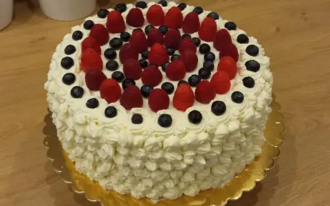Pyszny tort bezglutenowy ozdobiony bitą śmietaną, malinami i borówkami. Idealny na każdą okazję, a przepis na niego jest prosty!